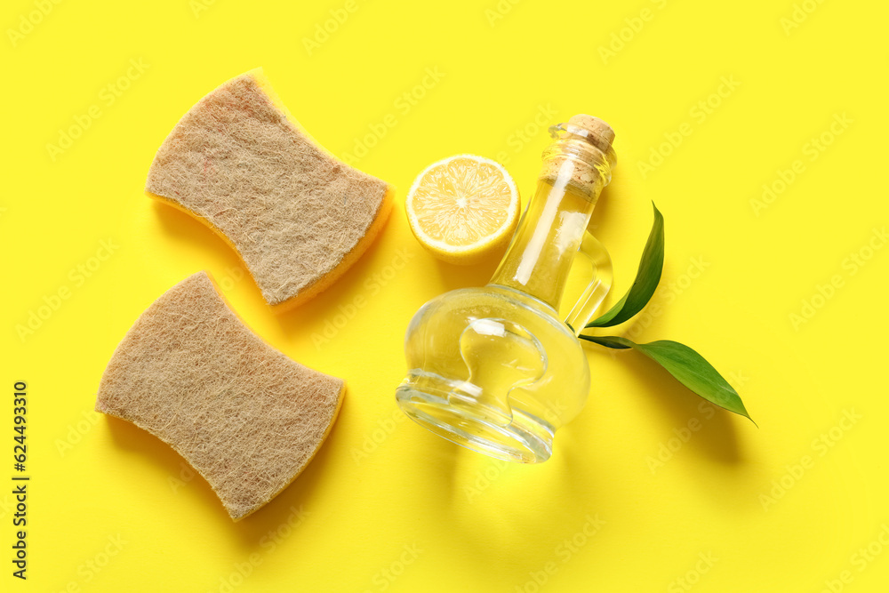 Jug of vinegar, sponges and lemon on yellow background