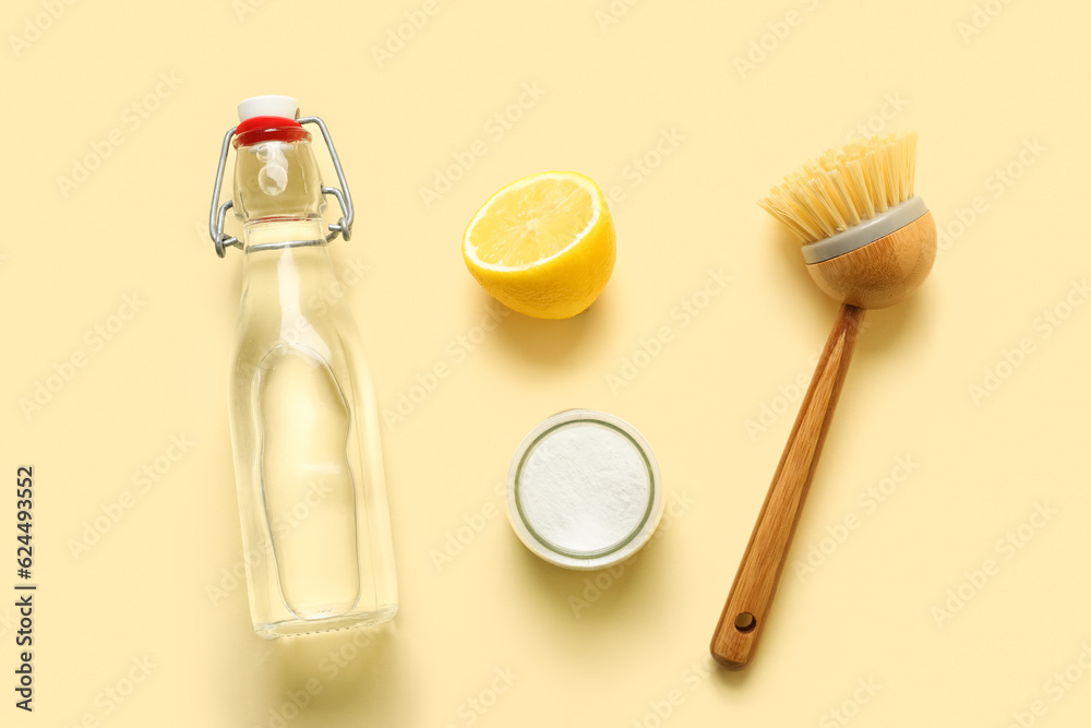 Bottle of vinegar, baking soda, brush and lemon on color background