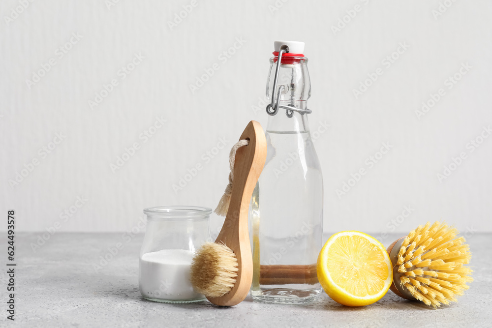 Bottle of vinegar, baking soda, brushes and lemon on table near light wall