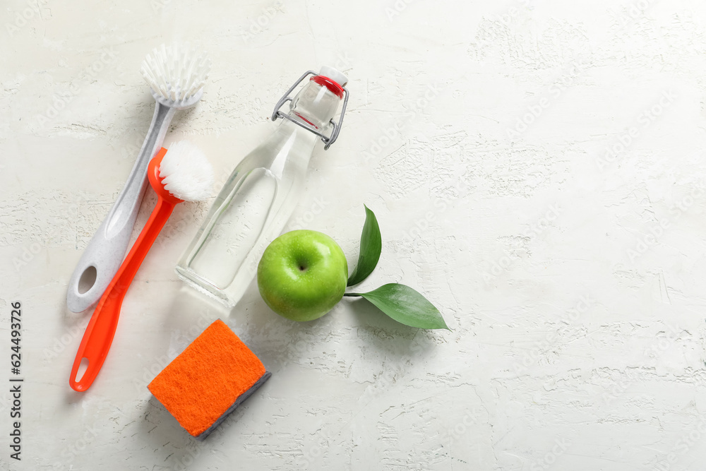 Bottle of vinegar, sponge, brushes and apple on light background