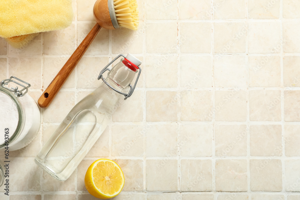 Bottle of vinegar, baking soda, sponge, lemon and brush on light tile background