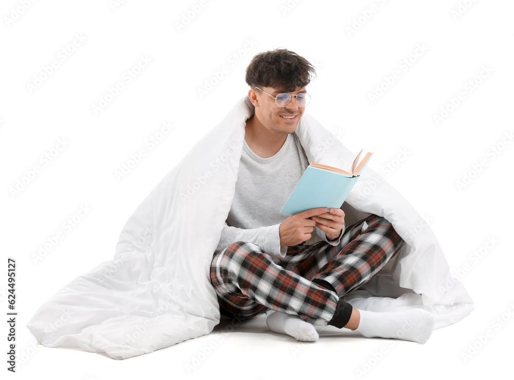 Handsome happy young man in eyeglasses with soft blanket reading book on white background