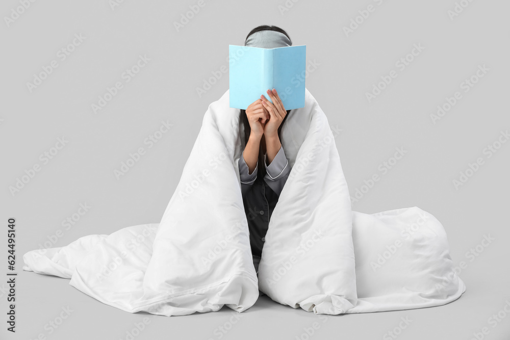 Beautiful young woman with soft blanket reading book on grey background