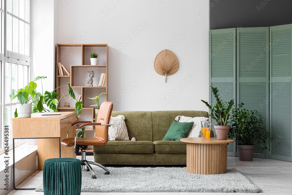 Interior of stylish living room with cozy green sofa and comfortable workplace near big window