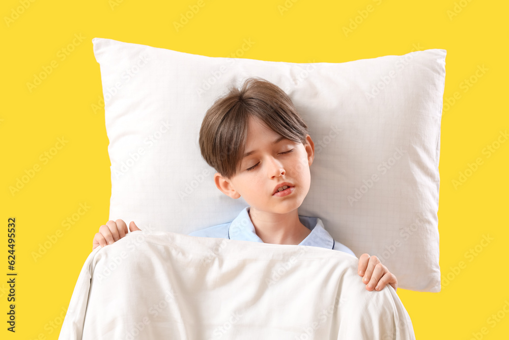 Sleeping little boy with pillow and blanket on yellow background, top view