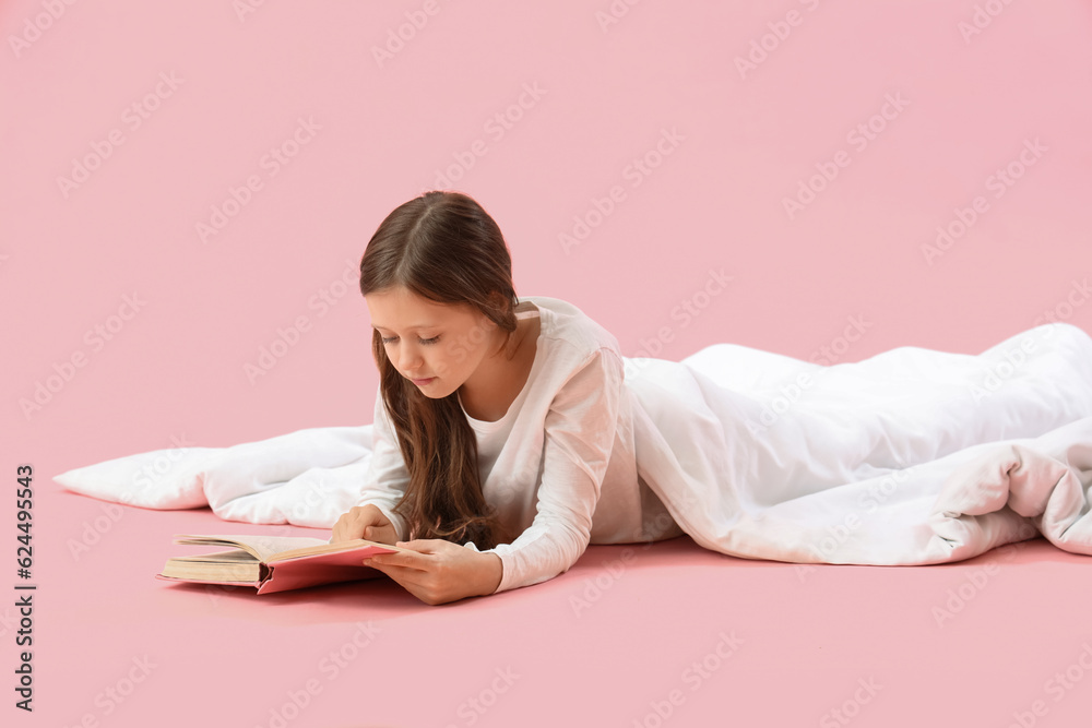 Little girl with blanket reading book on pink background