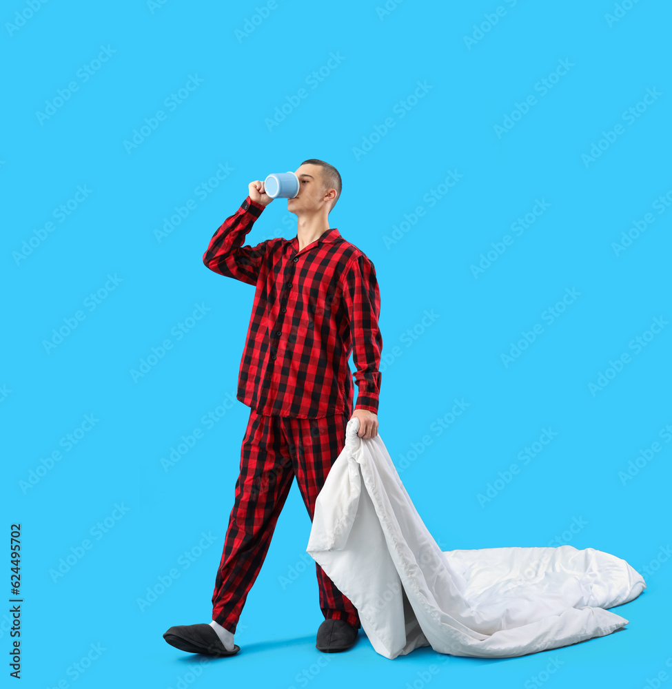 Young man with blanket drinking coffee on blue background