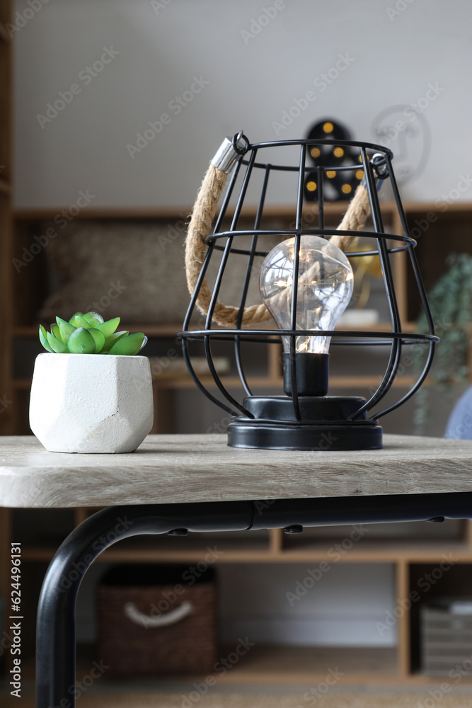 Glowing lamp with succulent on table in living room, closeup