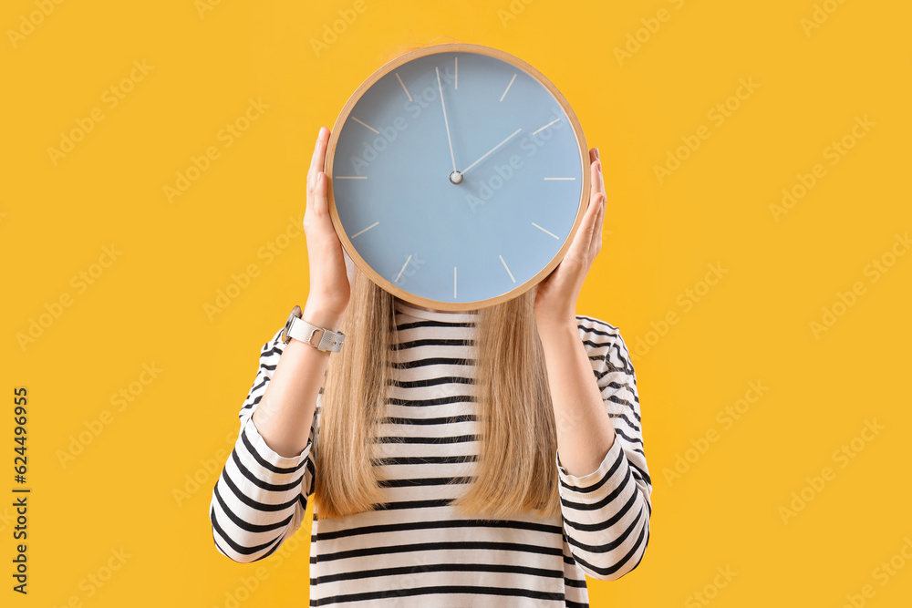 Young woman with clock on yellow background. Deadline concept