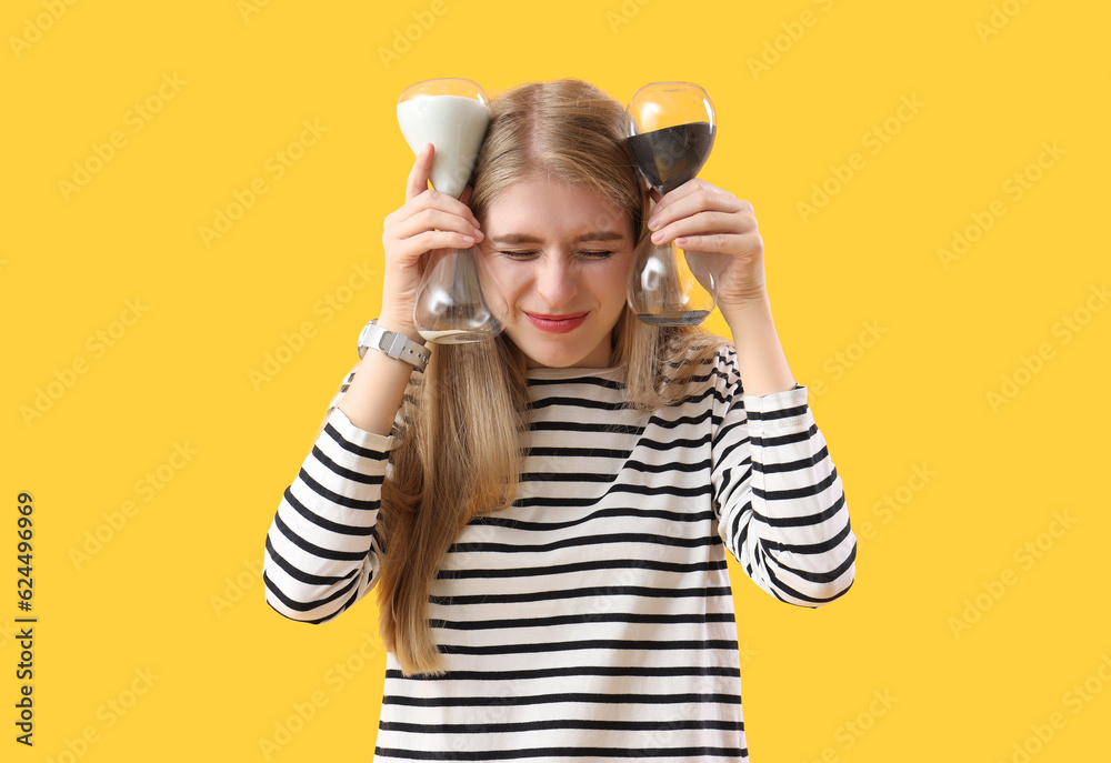 Stressed young woman with hourglass on yellow background. Deadline concept