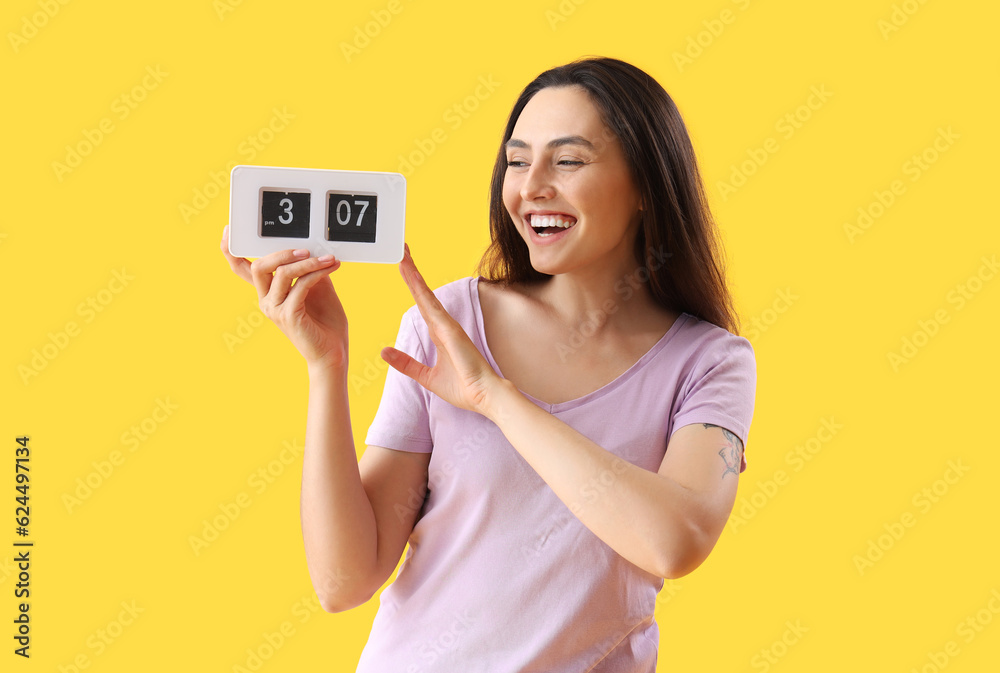 Young woman with clock on yellow background. Deadline concept