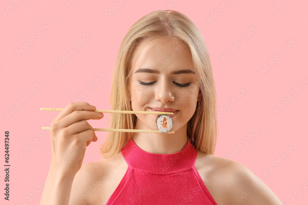 Young woman with tasty sushi roll on pink background, closeup