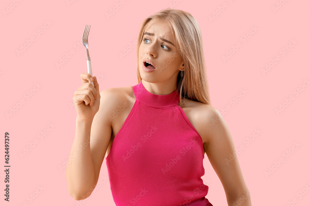 Shocked young woman with fork on pink background