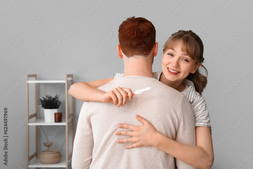 Happy young couple with pregnancy test hugging at home