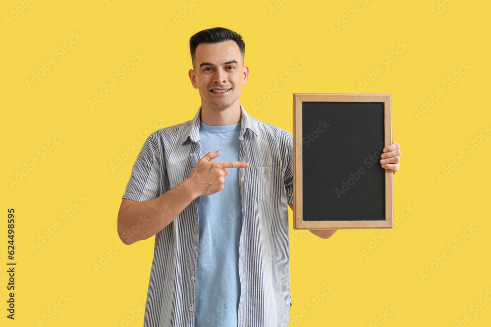 Male teacher pointing at chalkboard on yellow background