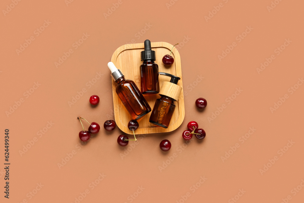 Wooden board with bottles of cosmetic products and sweet cherry on color background