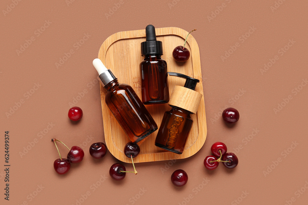 Wooden board with bottles of cosmetic products and sweet cherry on color background