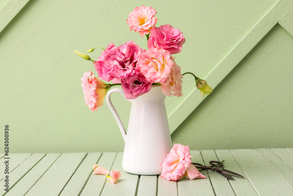 Jug with beautiful pink eustoma flowers on green wooden table