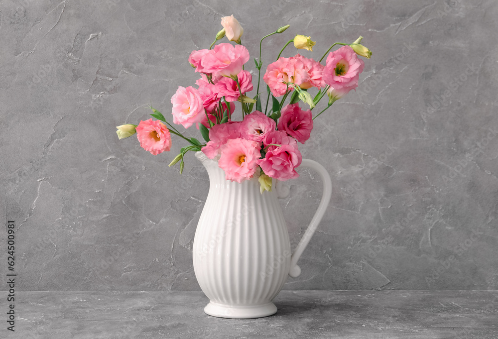 Jug with beautiful pink eustoma flowers on grey background