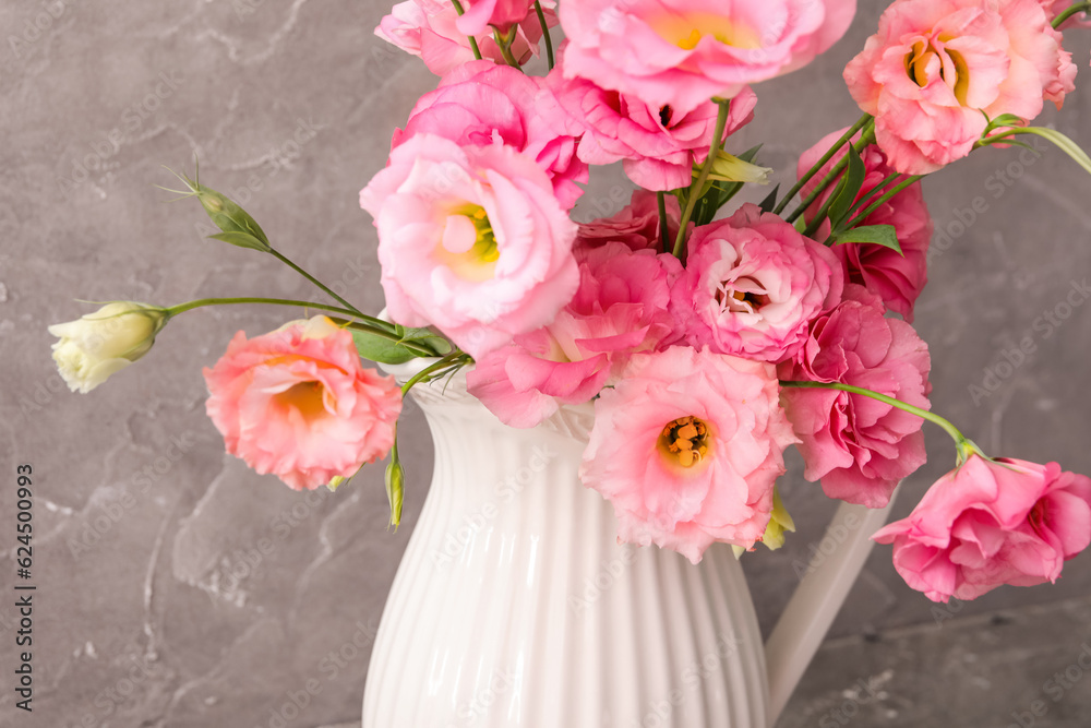 Jug with beautiful pink eustoma flowers on grey background