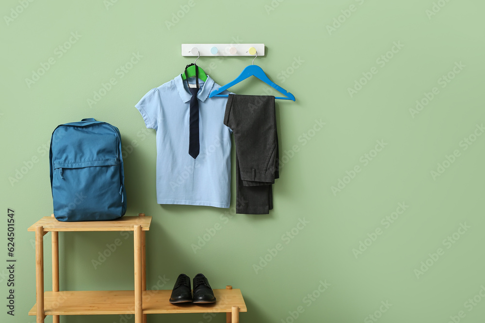 Stylish school uniform hanging on rack with backpack against green wall