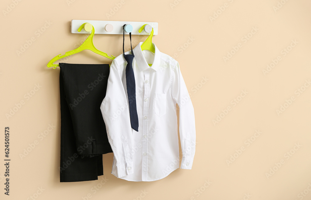 Stylish school uniform hanging on rack against beige wall