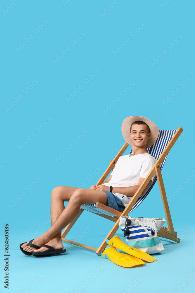 Teenage boy in deck chair on blue background