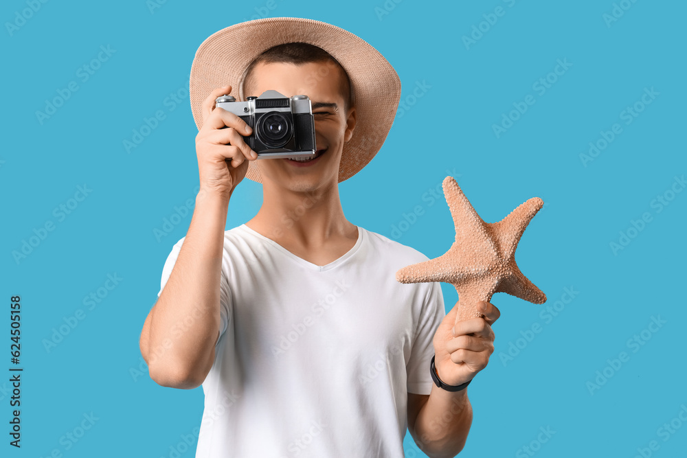 Teenage boy with photo camera and starfish on blue background