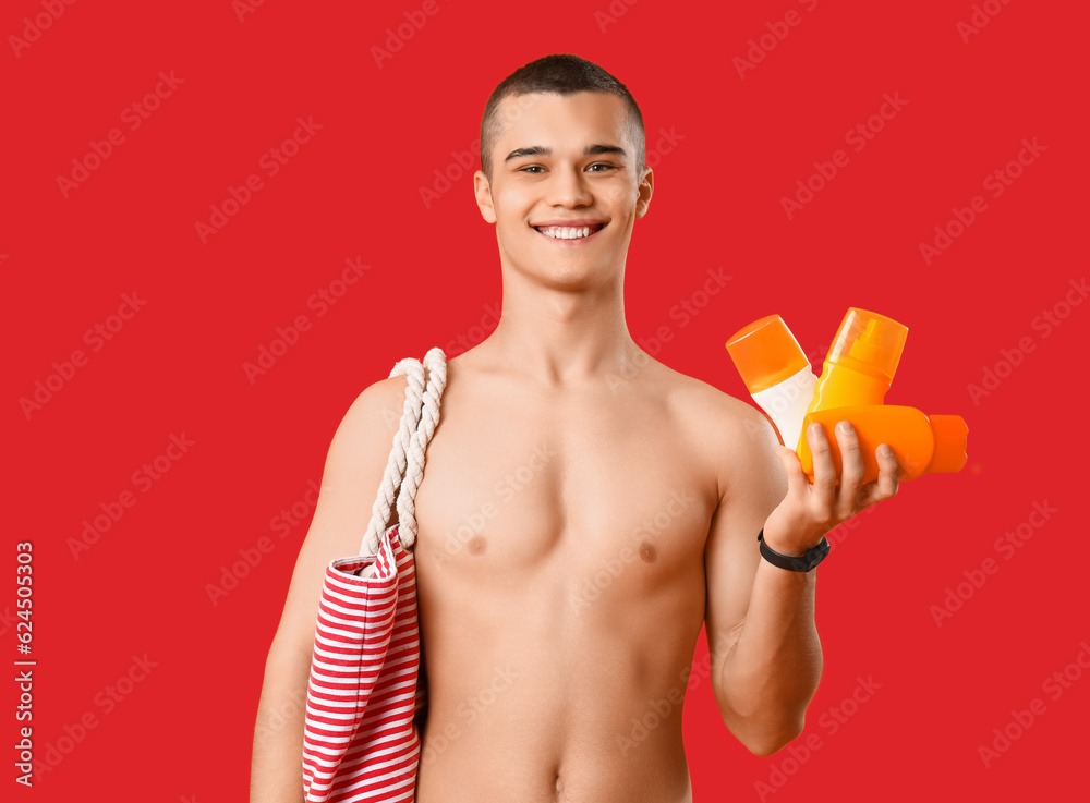 Teenage boy with bottles of sunscreen cream on red background