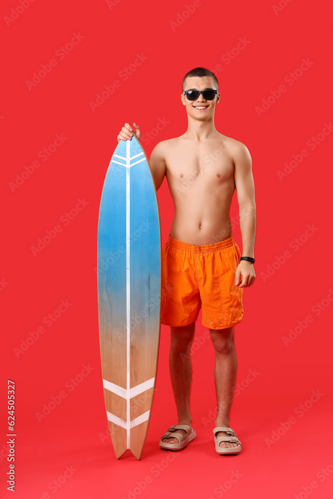 Teenage boy with surfboard on red background