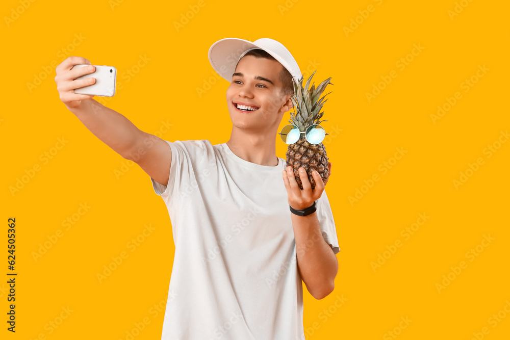 Teenage boy with pineapple taking selfie on yellow background