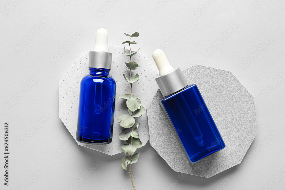 Composition with bottles of essential oil, podiums and eucalyptus branch on light background