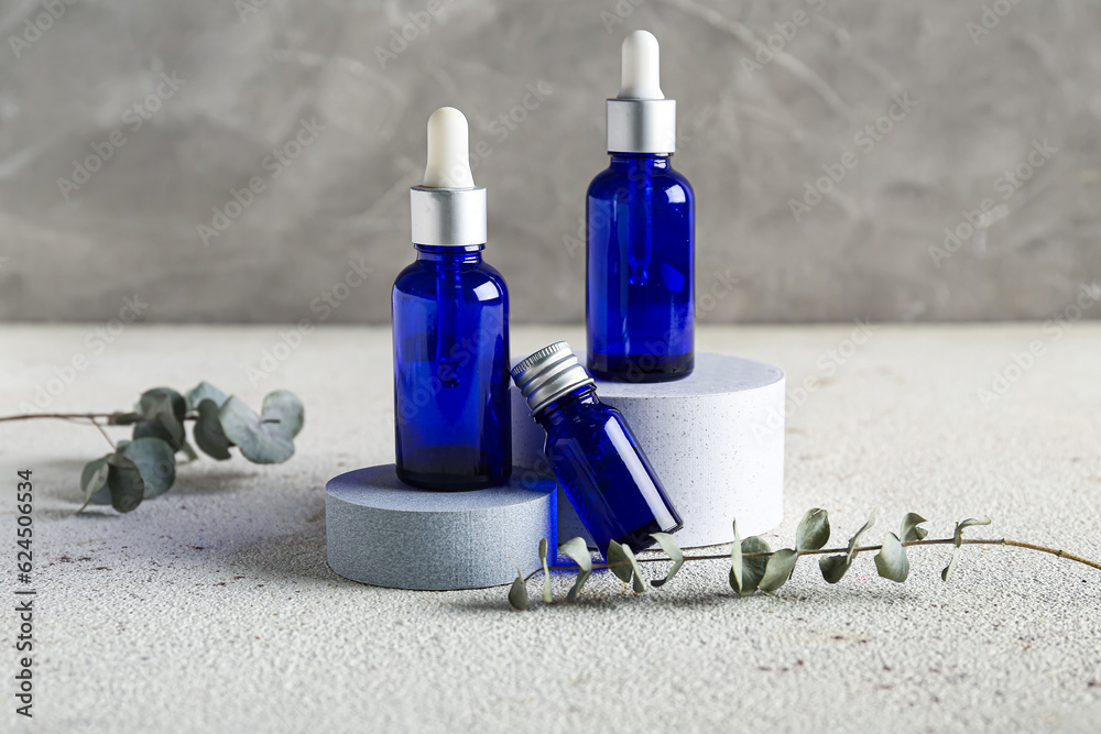 Composition with bottles of essential oil, podiums and eucalyptus branches on light table