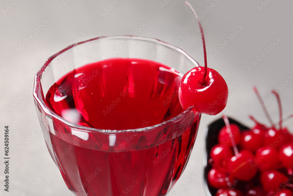 Glass of tasty cocktail with maraschino cherry on grey background