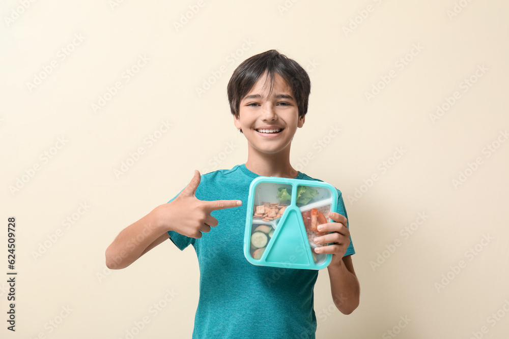 Little boy pointing at lunchbox on beige background