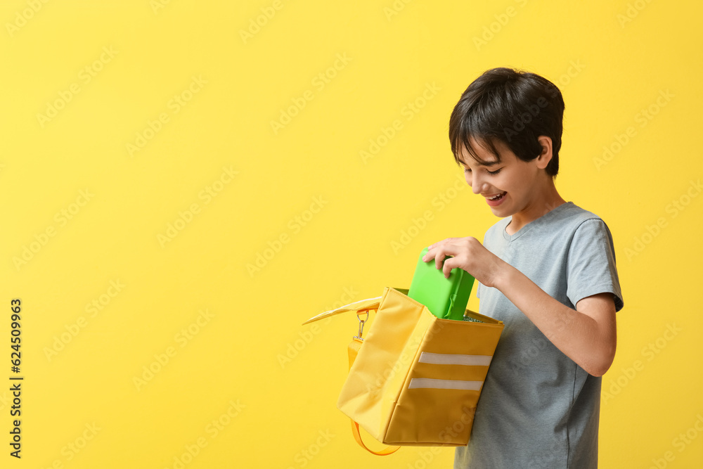 Little boy with lunchbox in bag on yellow background