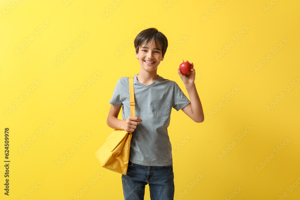 Little boy with lunch box bag and apple on yellow background