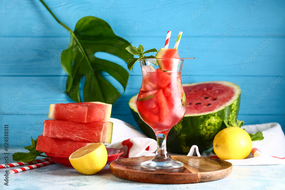 Glass of fresh watermelon lemonade with and palm leaf mint on blue table