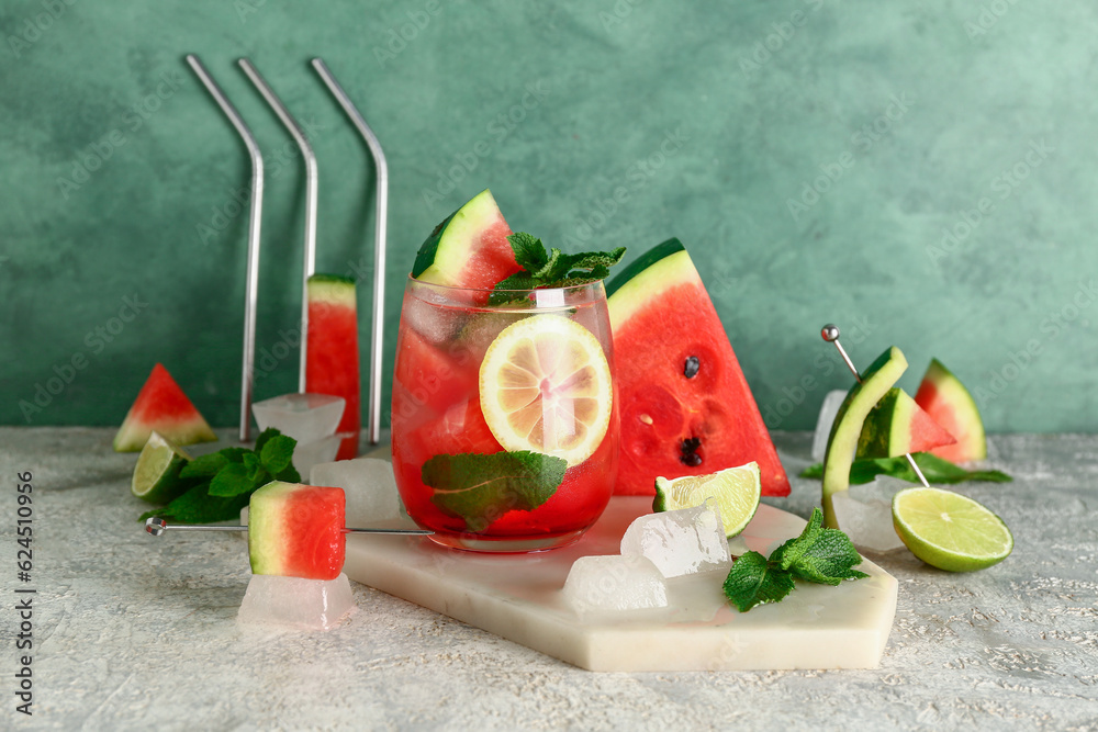 Board with glass of fresh watermelon lemonade and mint on grey table