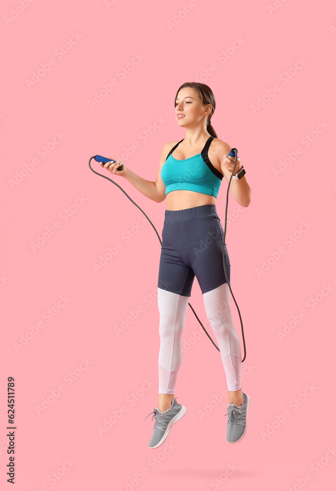 Sporty young woman jumping rope on pink background