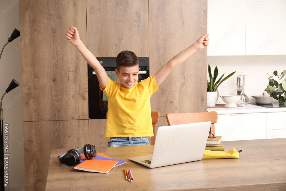 Happy little boy studying online with laptop in kitchen