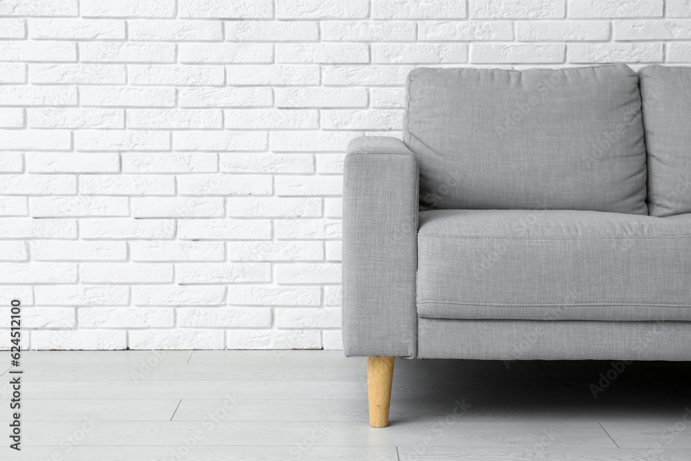 Cozy grey sofa near white brick wall