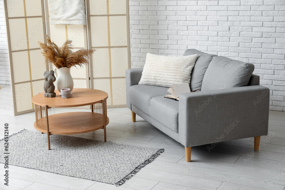 Cozy grey sofa, coffee table and folding screen near white brick wall