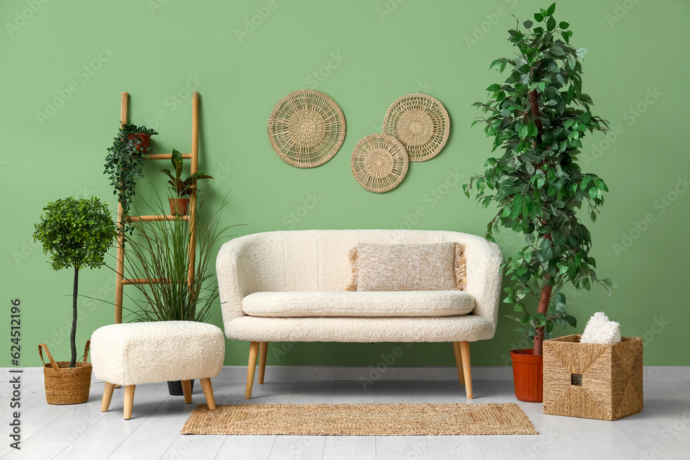 Cozy white sofa, ottoman and plants near green wall