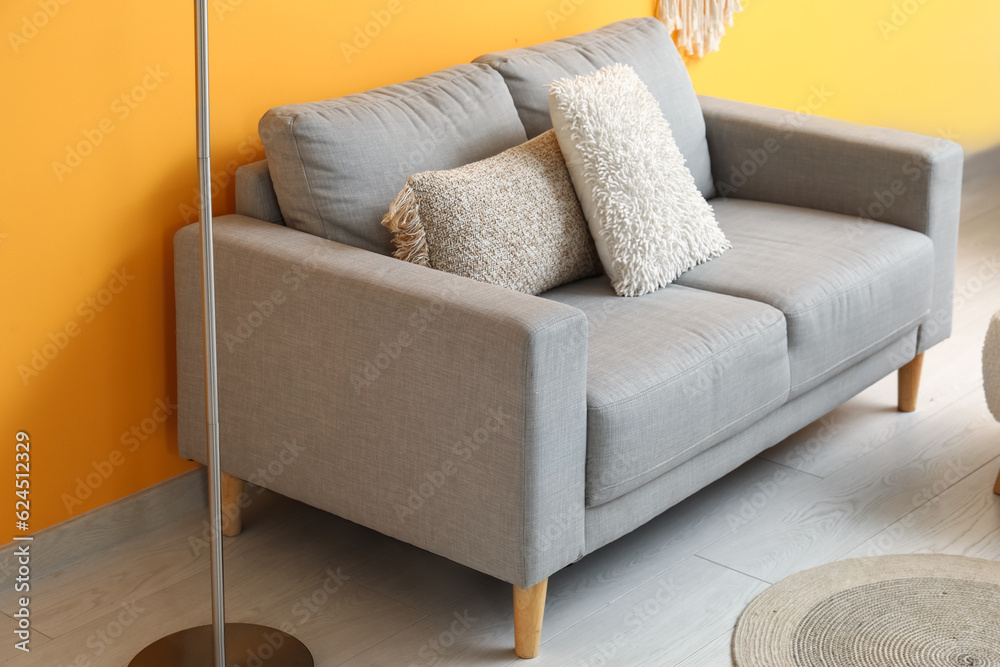 Cozy grey sofa with pillows near orange wall