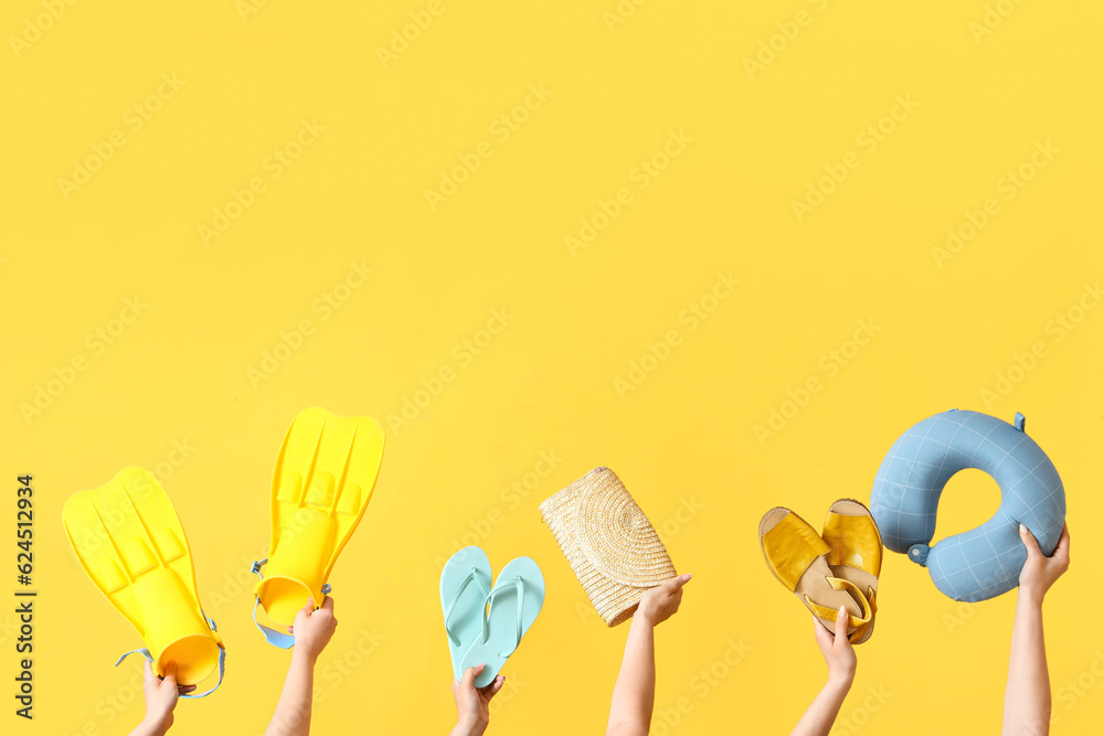 Many hands holding different beach accessories on yellow background