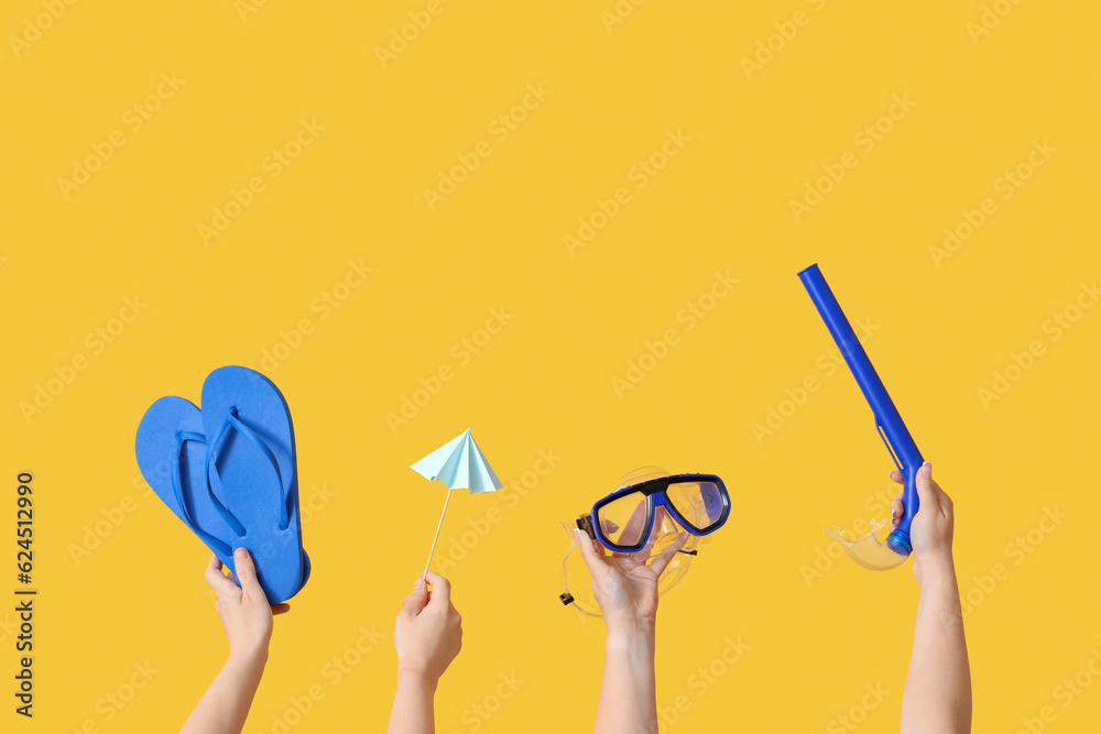 Many hands holding beach accessories on yellow background