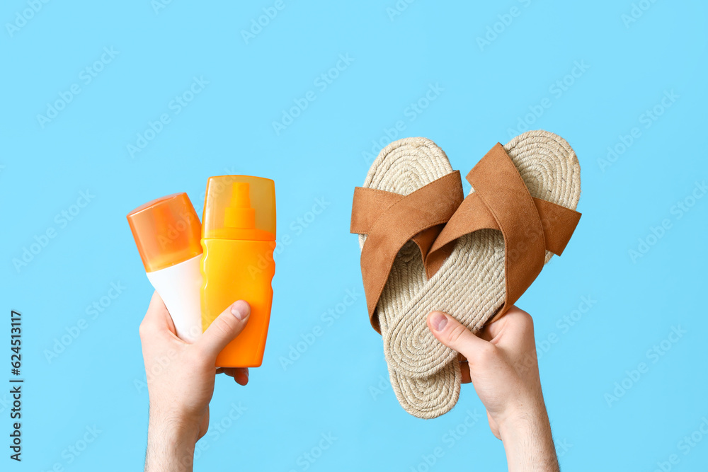 Male hands with flip flops and bottles of sunscreen cream on blue background