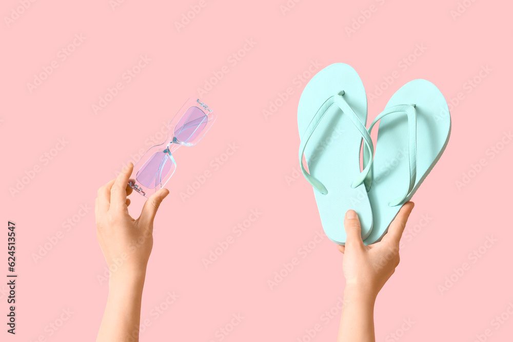 Female hands with flip flops and sunglasses on pink background