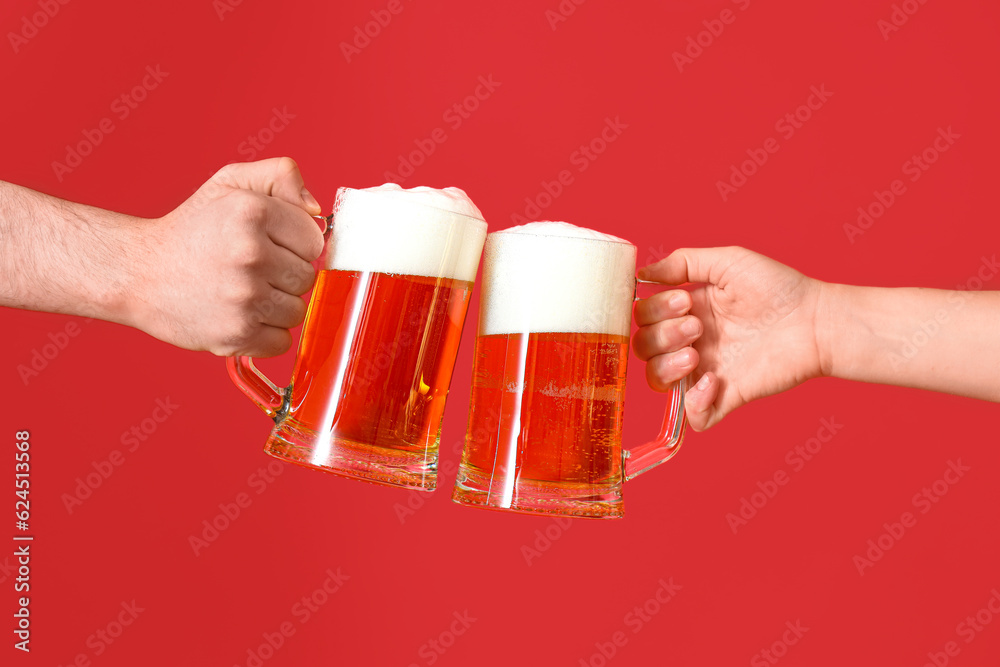 Man and woman with mugs of cold beer clinking on red background